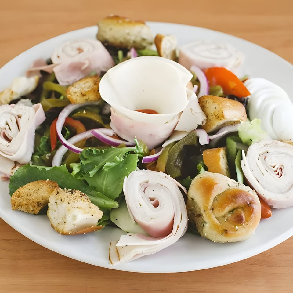 A vibrant salad with rolled deli meats, croutons, red onion, and bell peppers on a white plate.