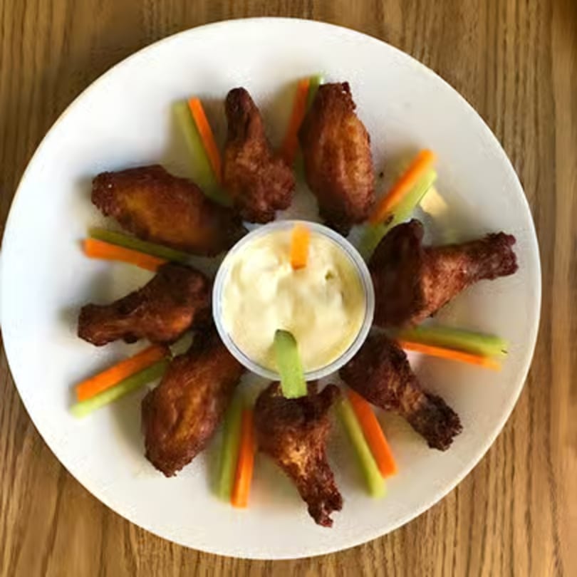 A white plate of Bella Luna Pizza's crispy chicken wings, with celery, carrots, and dipping sauce.