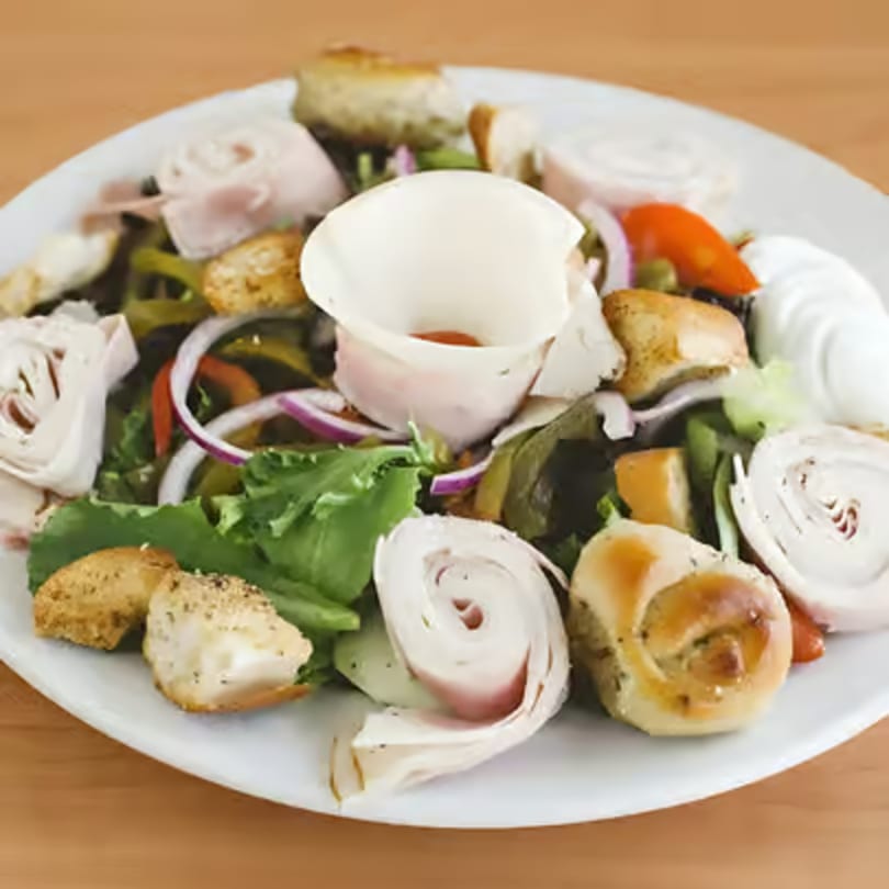 A fresh salad with lettuce, red onions, bell peppers, croutons, and rolled deli meat.