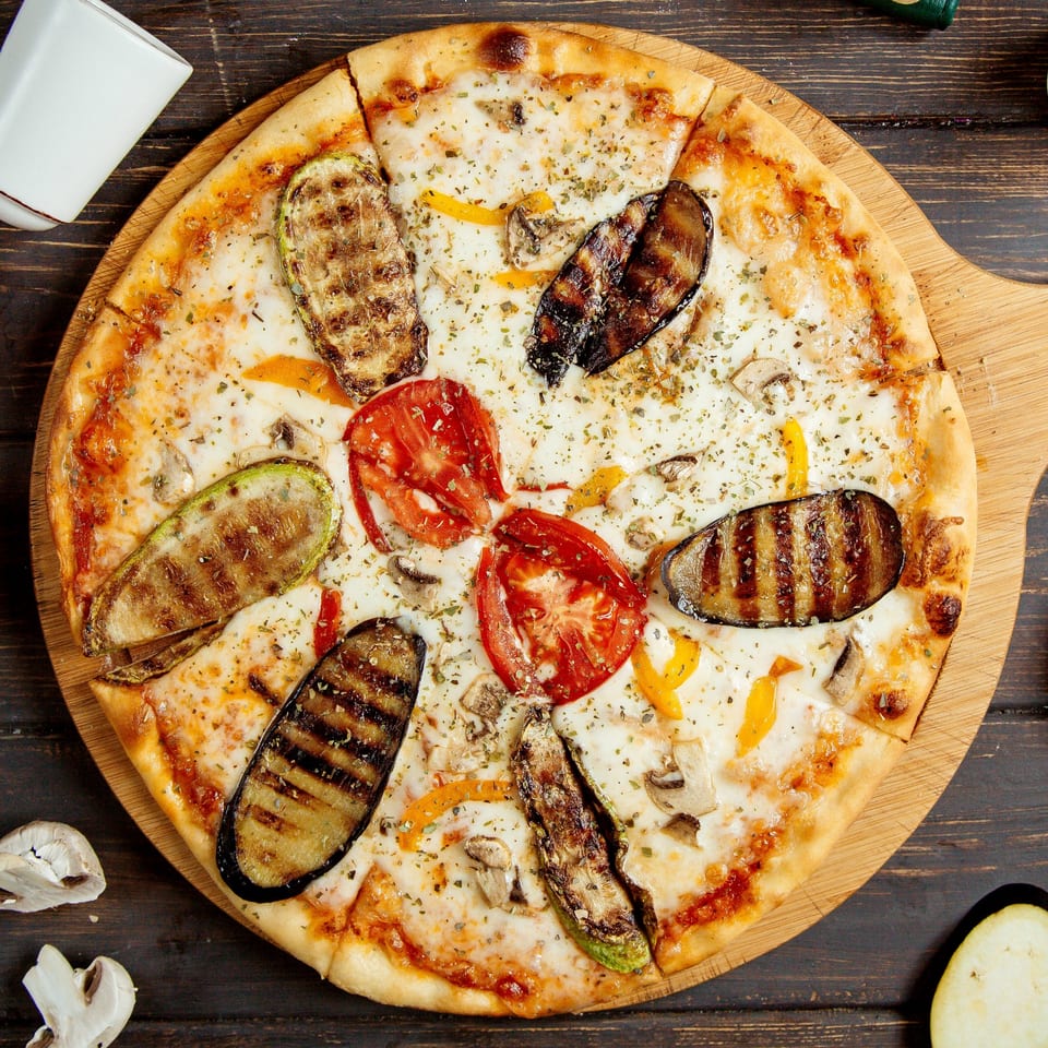 Bella Luna Pizza's vegetarian pizza with grilled zucchini, eggplant, tomatoes, and mushrooms on a wooden board.
